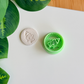 Spiral seashell clay cutter and its white clay impression on a white surface next to green leaves.