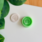 Seashell clay cutter and its white clay impression on a white surface next to green leaves.