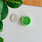 A top-down view of a mint green 3D-printed circular clay cutter featuring an anchor emblem and a rope-textured border, paired with a white polymer clay disc showing the crisp, embossed impression of the same nautical design on a clean white surface.
